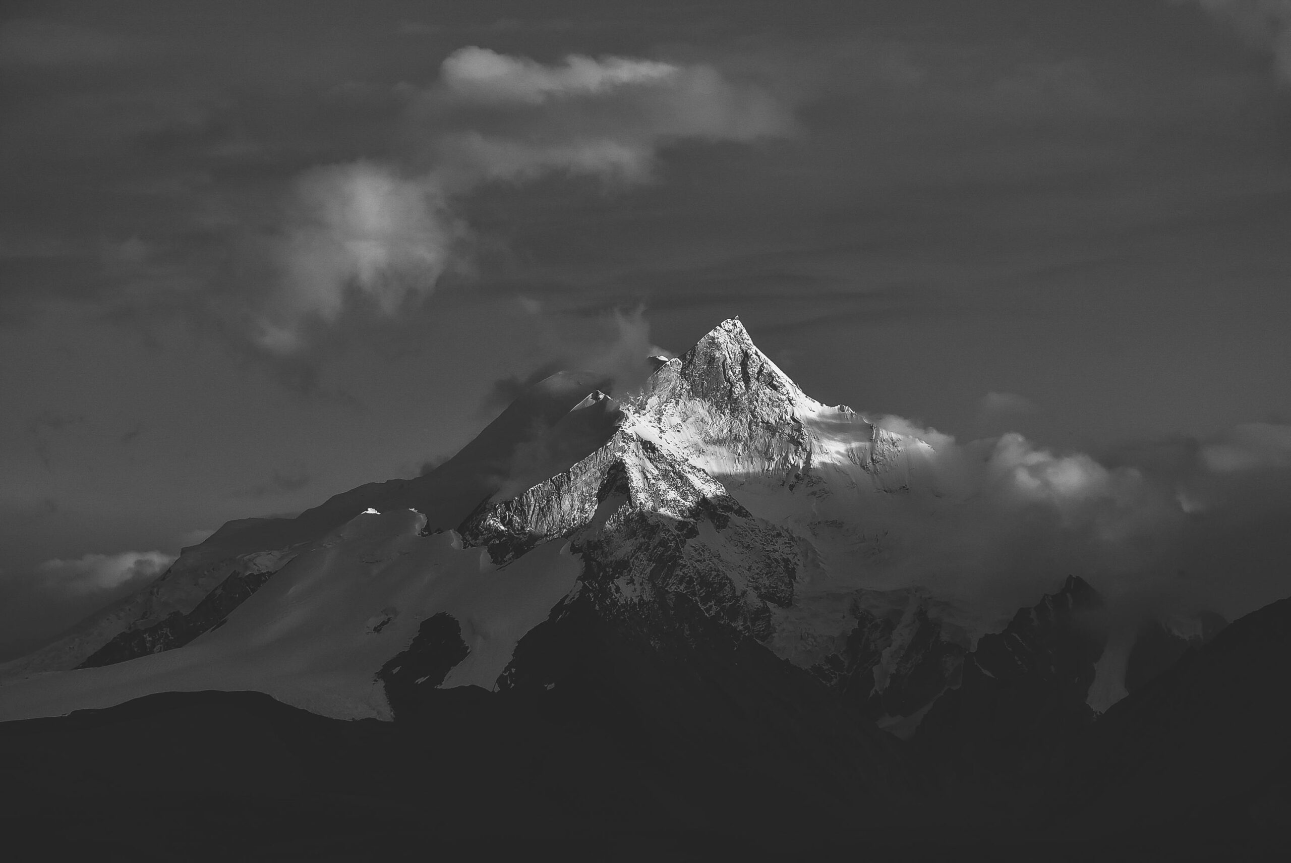 Stunning black and white image of a snow-capped mountain peak in Tibet, enveloped in clouds.
